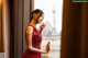 A woman in a red dress standing by a window.