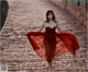 A woman in a red dress is dancing on a brick walkway.