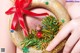 A woman's hand holding a gold wreath with a red bow.