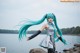 A woman with long blue hair standing on a rock by the water.